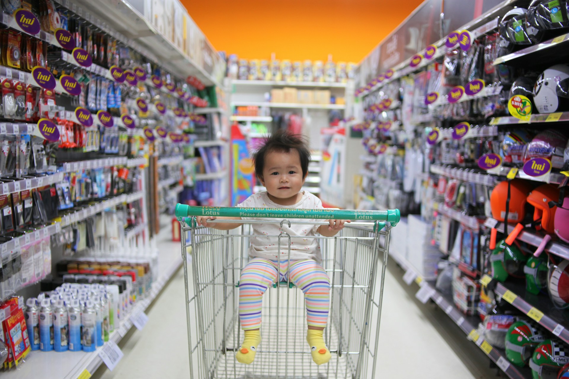 Little child in a grocery cart, in a grocery aisle, smiling at the camera