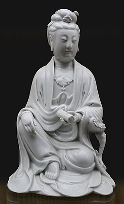 An ancient statue of Quan Yin, seated and with flowing robes and a scroll in her hand