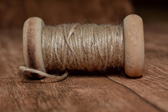 Light brown thick string wrapped around a wooden spool on its side on a wooden floor