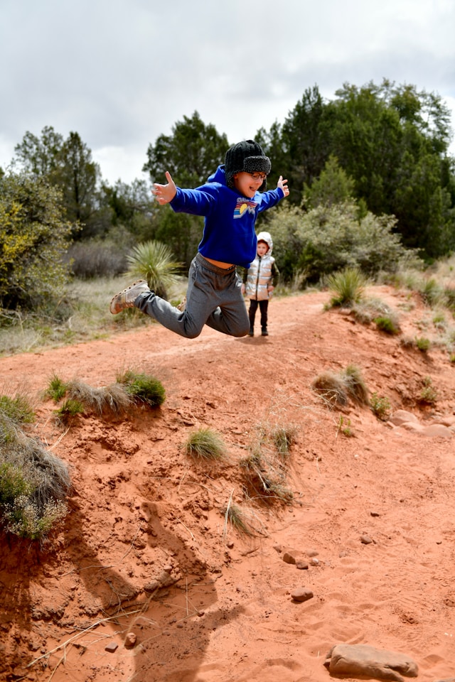 Young boy joyfully leaping off a small hill, a if he's flying through the air.